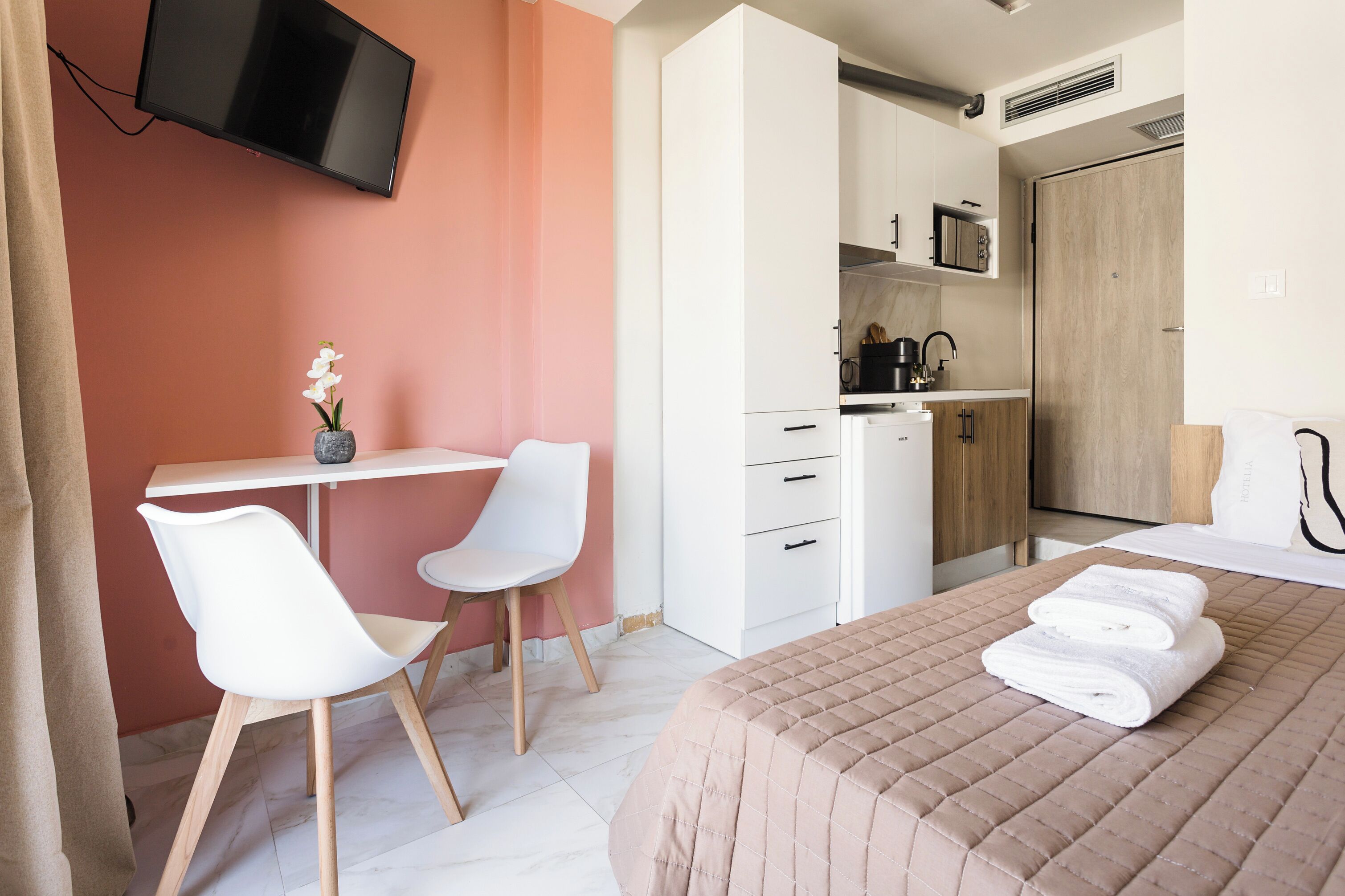 Ein Hotelzimmer mit einem Bett, einem Schreibtisch mit Stuhl, einem an der Wand montierten Fernseher und einer Küchenzeile.