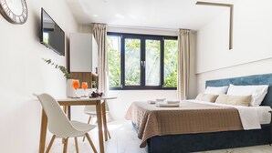 A bedroom with a bed, a desk with a chair, a TV, and a window with curtains.