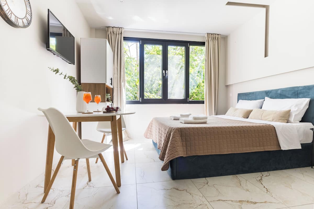 Une chambre à coucher avec un lit, un bureau avec une chaise, une télévision et une fenêtre avec des rideaux.