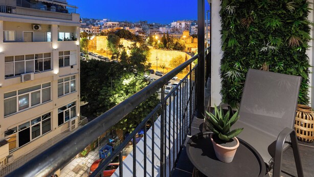 A balcony with a potted plant, a chair, and a view of a cityscape at dusk.