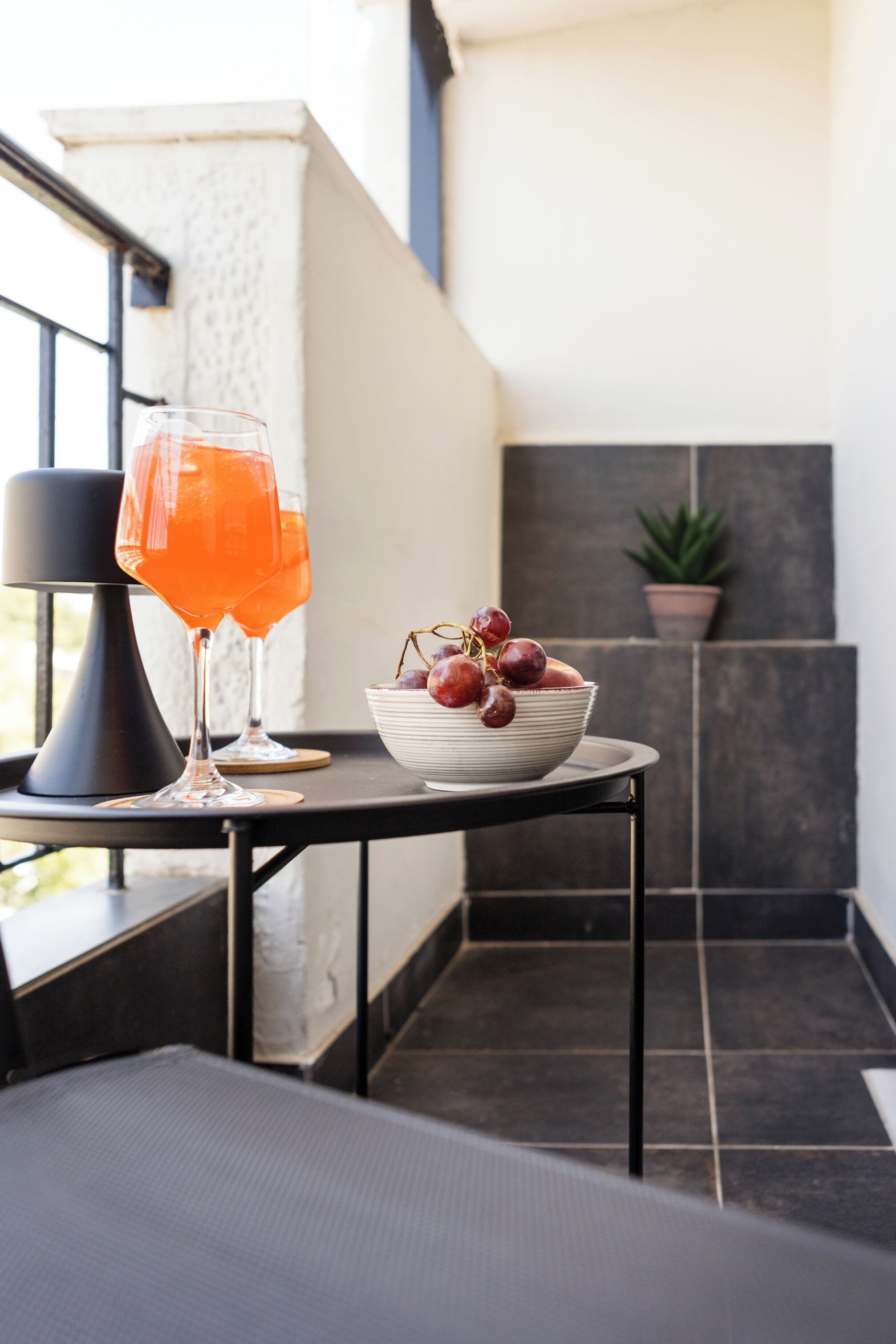 A table with a glass of orange drink, a bowl of grapes, and a potted plant in a modern setting.