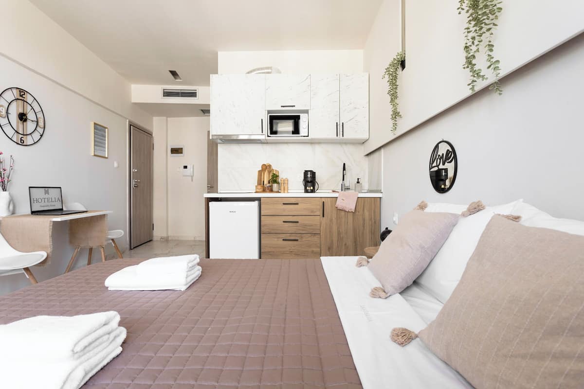 Une chambre d’hôtel moderne équipée d’un lit, d’un bureau, d’une kitchenette et d’une horloge murale.