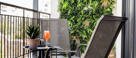 Ein Balkon mit Tisch, Stühlen, einem Topfpflanzen und einem Glas Drink.