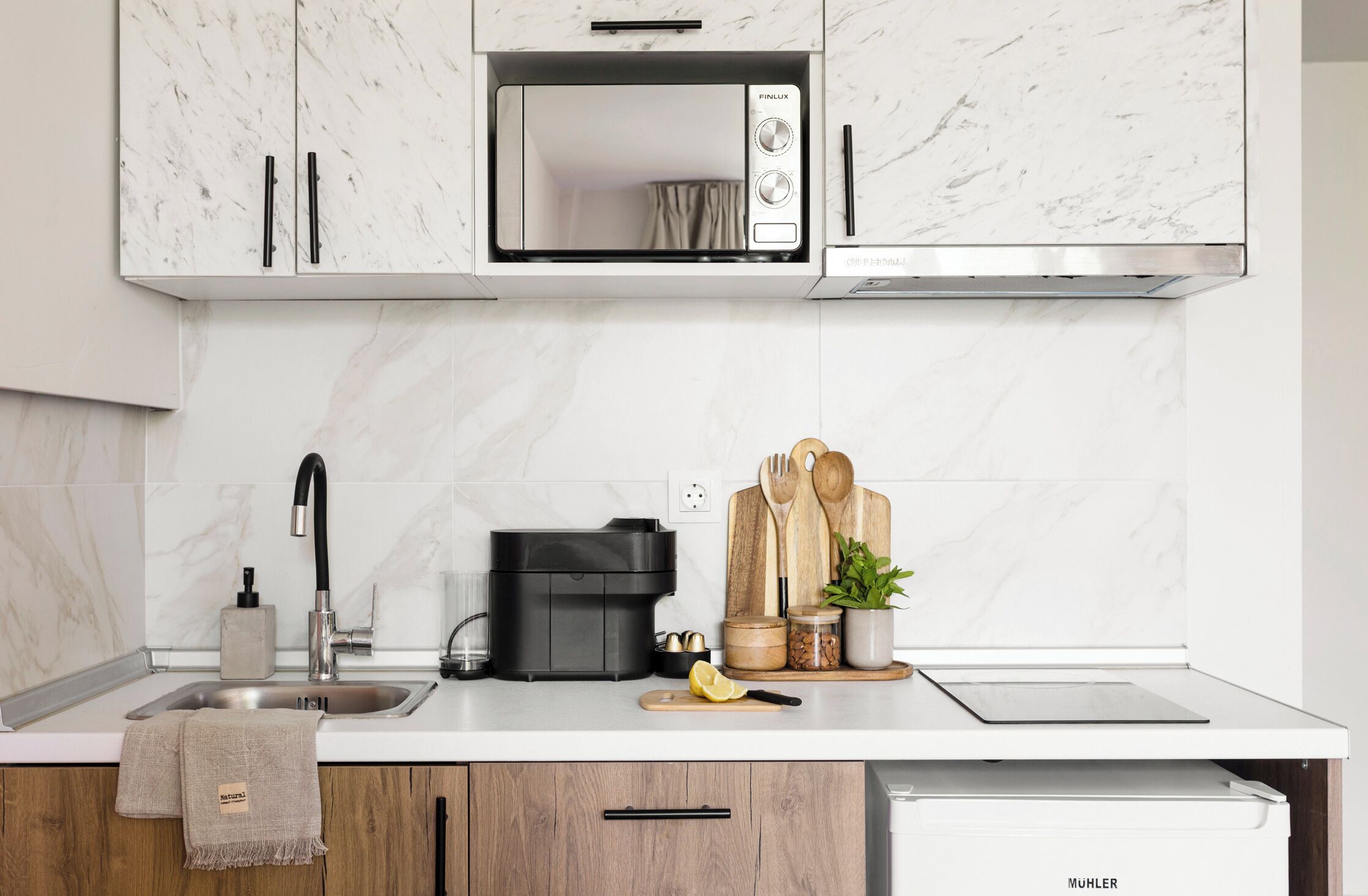 A modern kitchen with a built-in microwave, a sink with a faucet, a coffee maker, and wooden utensils on the counter.
