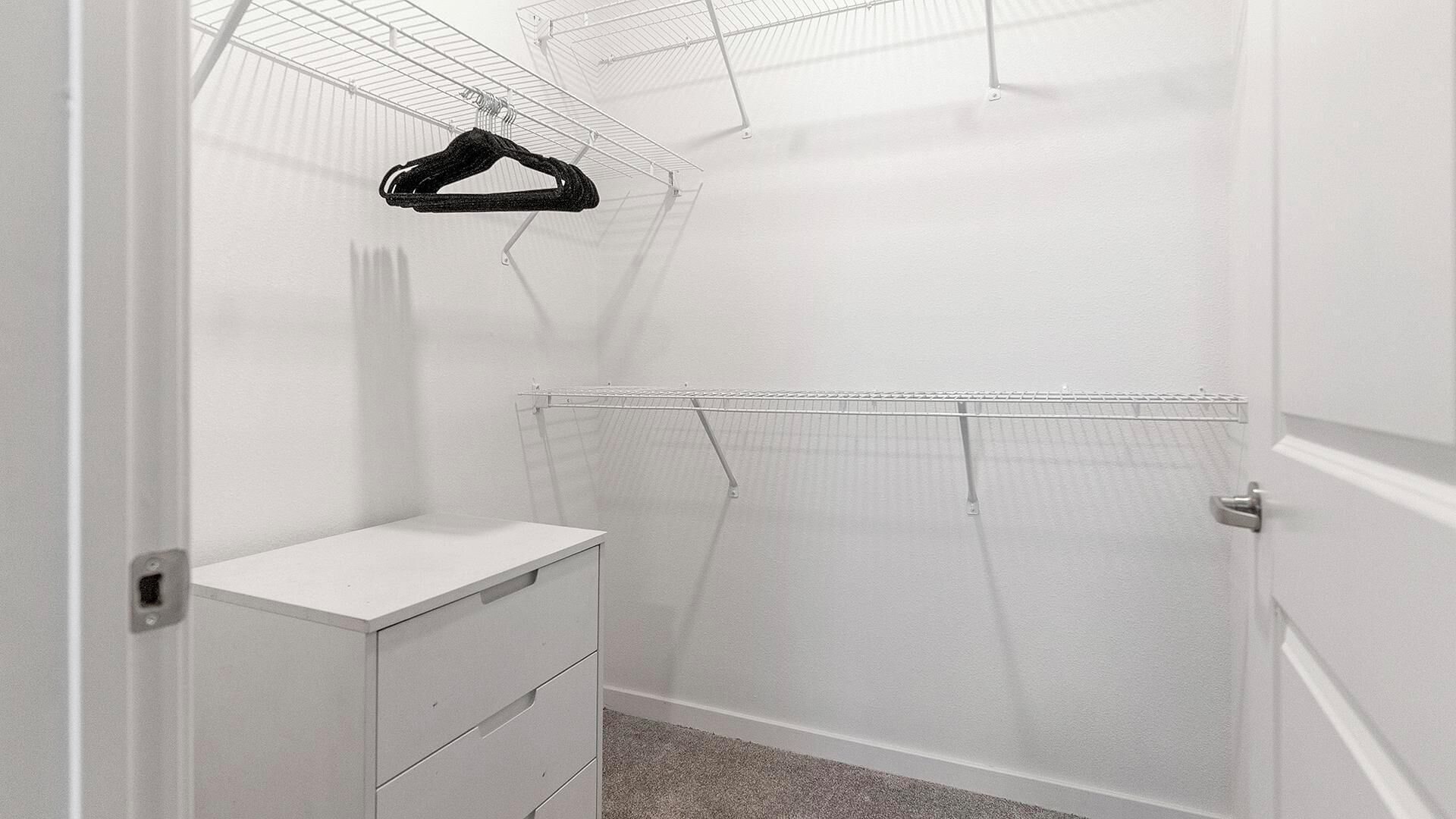 A walk-in closet with a white dresser, a hanging rack, and a wire shelving unit.