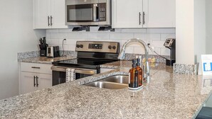 A modern kitchen with granite countertops, stainless steel appliances, and white cabinetry. - Landing | Spectacular 1BD, Pool, Yoga Studio (Cape Coral)
