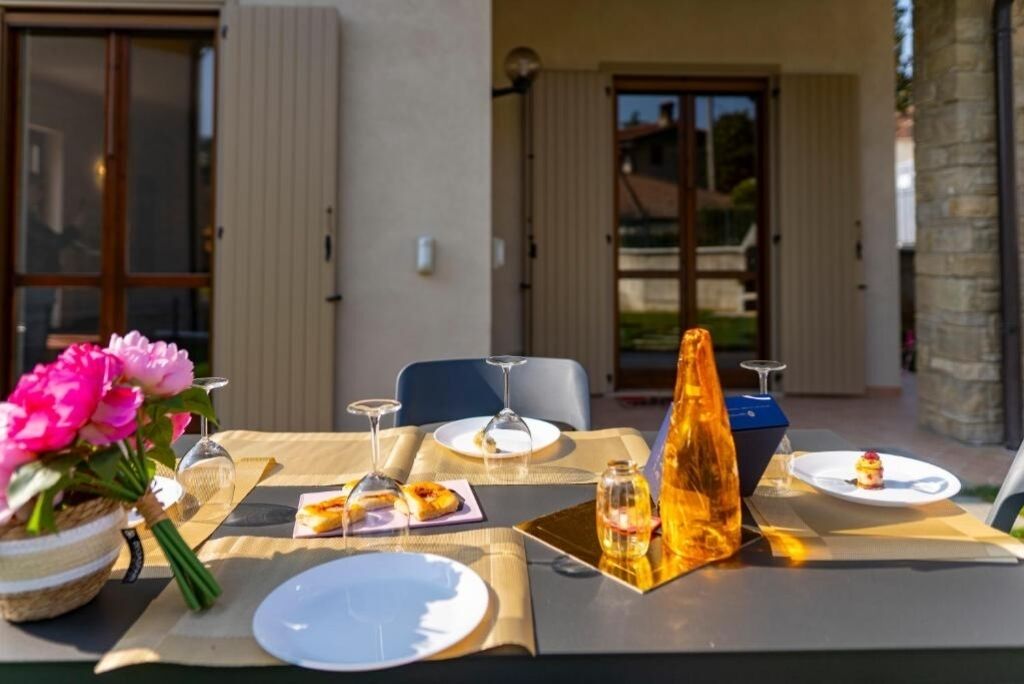 An outdoor dining area with a table set for two, featuring a bottle of wine, plates, and a small dessert.