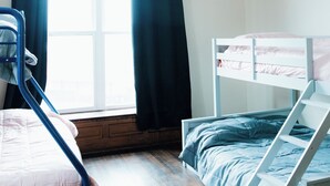 Un dormitorio con una cama litera, una ventana con cortinas y suelo de madera.