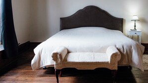 Una cama bien hecha con cabecera, una mesita de noche con lámpara y un banco al pie de la cama.