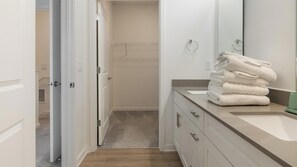 A bathroom with a vanity, a towel stack, and a shower area.