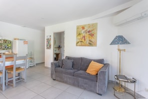 A living room with a grey sofa, a dining table with chairs, a floor lamp, and a painting on the wall. - Peaceful Country Escape with Mountain View, Wi-Fi, and Air Conditioning (Parbayse)