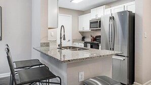 A compact kitchen with a stainless steel refrigerator, a microwave, and a sink. - Landing at Vantage - 2 Bedrooms in Hancock (Cape Coral)