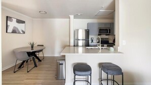 A modern kitchen with a central island, stainless steel appliances, and a dining area with a table and chairs. - Landing | Amazing 2BD, Gym, Game Room (Murfreesboro)