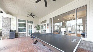 A ping pong table in an outdoor area with a brick floor, a ceiling fan, and large windows. - Landing | Amazing 2BD, Gym, Game Room (Murfreesboro)