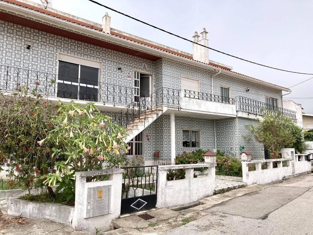 A two-story house with a tiled facade, a balcony, and a small garden area.