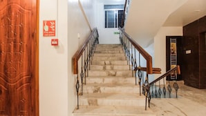A staircase with a wooden door on the left, a fire alarm pull station, and an EXIT sign above the stairs. - Grande Inn (Erode)
