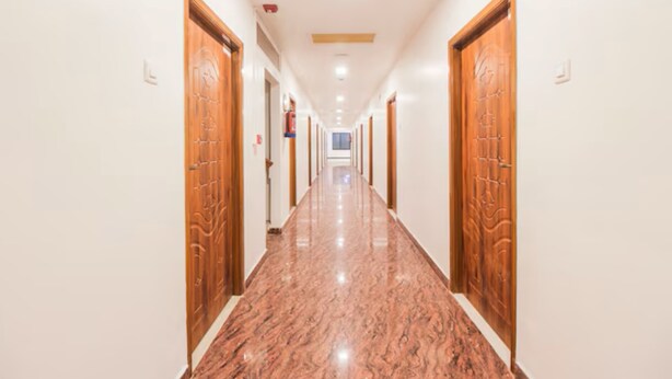 A long, narrow hallway with wooden doors on both sides and a polished marble floor. - Grande Inn (Erode)