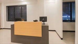 A reception desk with a wooden counter and a black monitor. - Grande Inn (Erode)