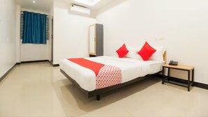 A hotel room with a bed, a bedside table, a mirror, and a window with curtains. - Grande Inn (Erode)