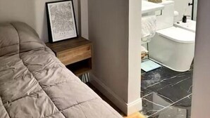 A bedroom with a bed, a bedside table with a framed picture, and a view into a bathroom with a toilet and a mirror. - Apartment in Almagro (Near Parque Centenario and Hospital Italiano) (CABA)