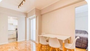 A room with a wooden herringbone floor, a white dining table with four chairs, and a grey bed in the corner. - Apartment in Almagro (Near Parque Centenario and Hospital Italiano) (CABA)