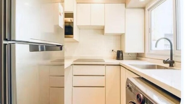 A compact kitchen with a stainless steel refrigerator, a built-in oven, a dishwasher, and a window providing natural light. - Apartment in Almagro (Near Parque Centenario and Hospital Italiano) (CABA)