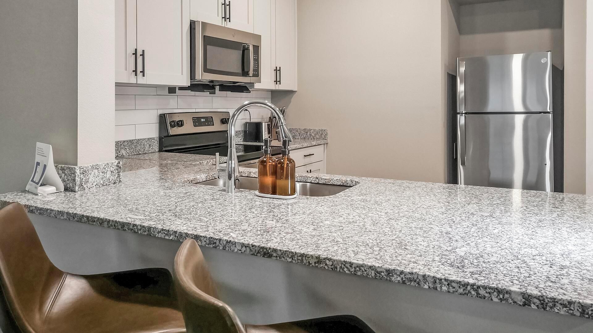 A kitchen with white cabinets, a stainless steel refrigerator, a microwave, and a granite countertop.