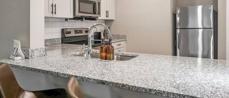 A kitchen with white cabinets, a stainless steel refrigerator, a microwave, and a granite countertop.