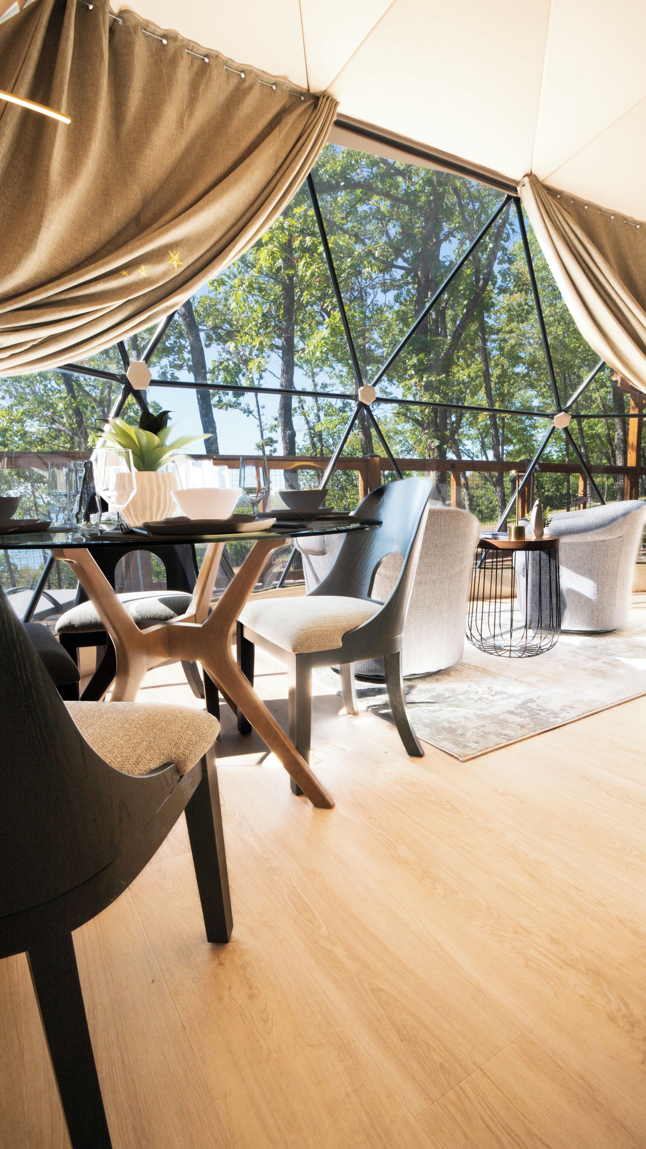 Un comedor con mesa de vidrio, sillas y vistas a árboles a través de una estructura de ventana geométrica.
