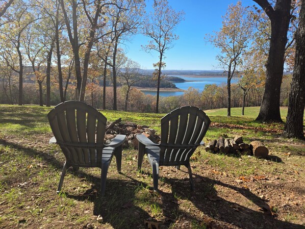 Twee Adirondack stoelen gericht op een meer met bomen op de achtergrond.