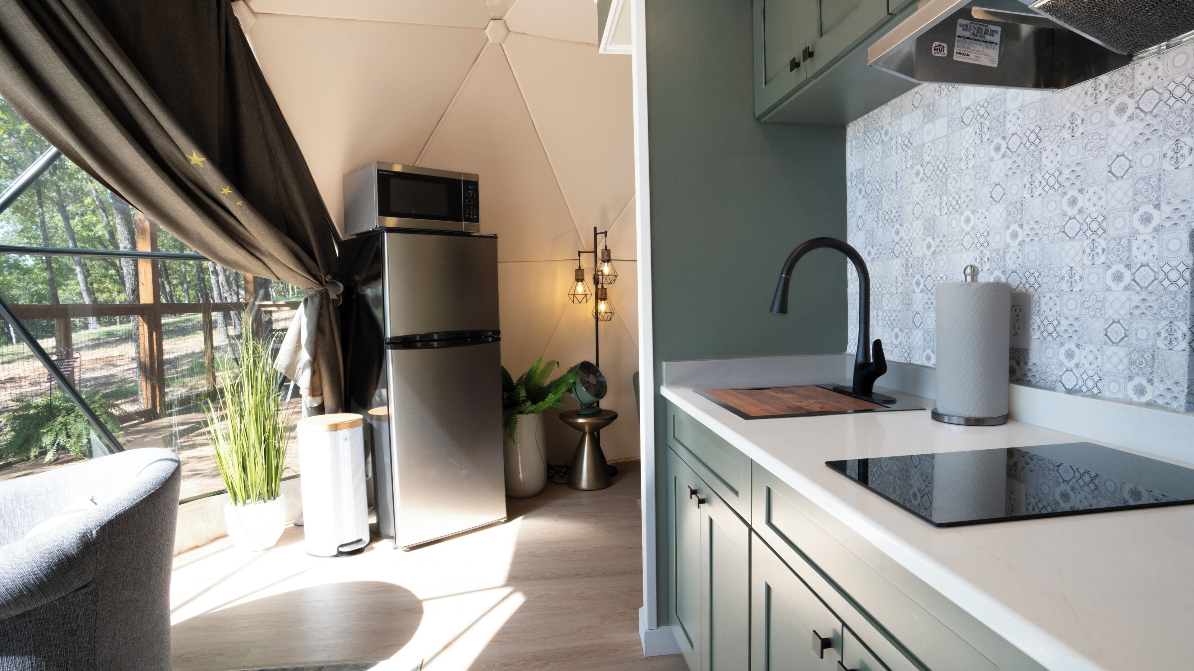 Cocina compacta con microondas integrado, lavamanos y ventana con vistas a zonas verdes.