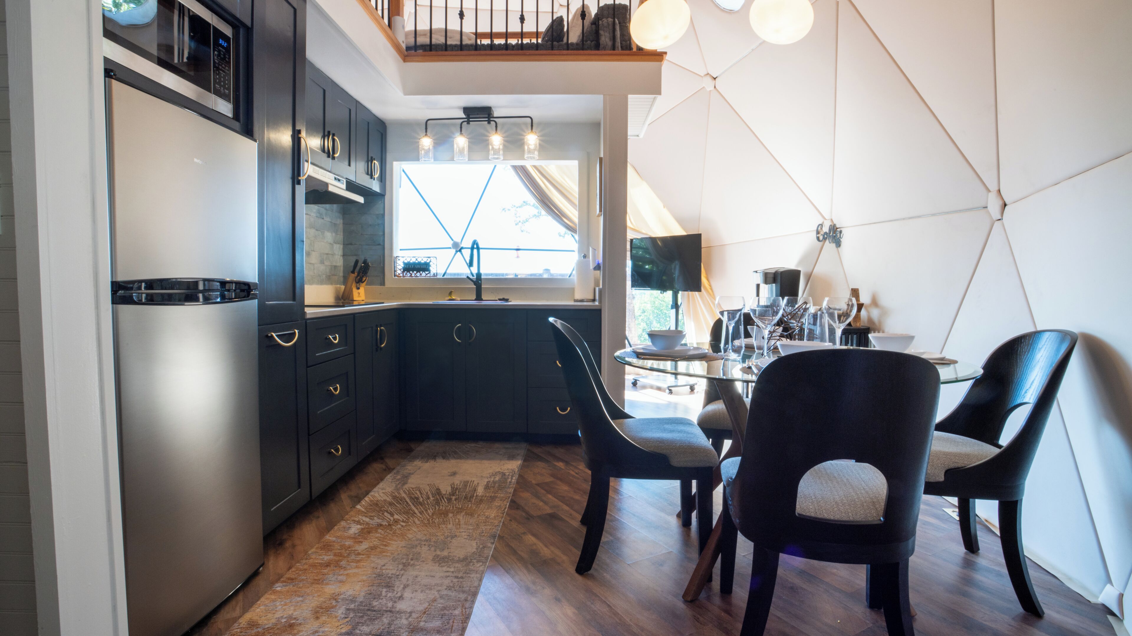 A modern kitchen with dark cabinets, a stainless steel refrigerator, and a dining area with two chairs and a table.
