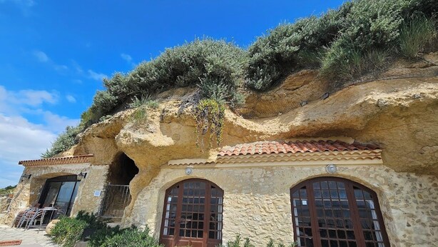 Un edificio de piedra con fachada rústica, que presenta un gran arco de entrada y dos ventanas con persianas de madera.