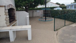 Un patio con una estructura de piedra, posiblemente una chimenea, una estructura para escalar con cuerdas y un área cercada.