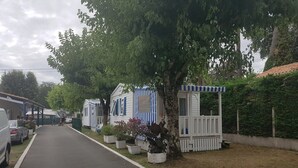 Una hilera de casas móviles con toldos a rayas blancas y azules, un camino pavimentado y un área verde con árboles.