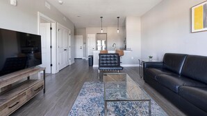 A modern living room with a flat-screen TV, a leather sofa, a glass coffee table, and a patterned rug.