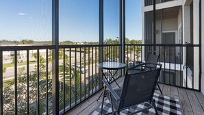 A balcony with a table and chairs, offering a view of a parking lot and greenery.