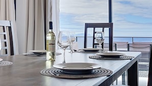 A dining table set with plates, glasses, and a bottle of wine, with a scenic view through large windows. - Blue Outlook Retreat by Atlantic Holiday (Santa Cruz)