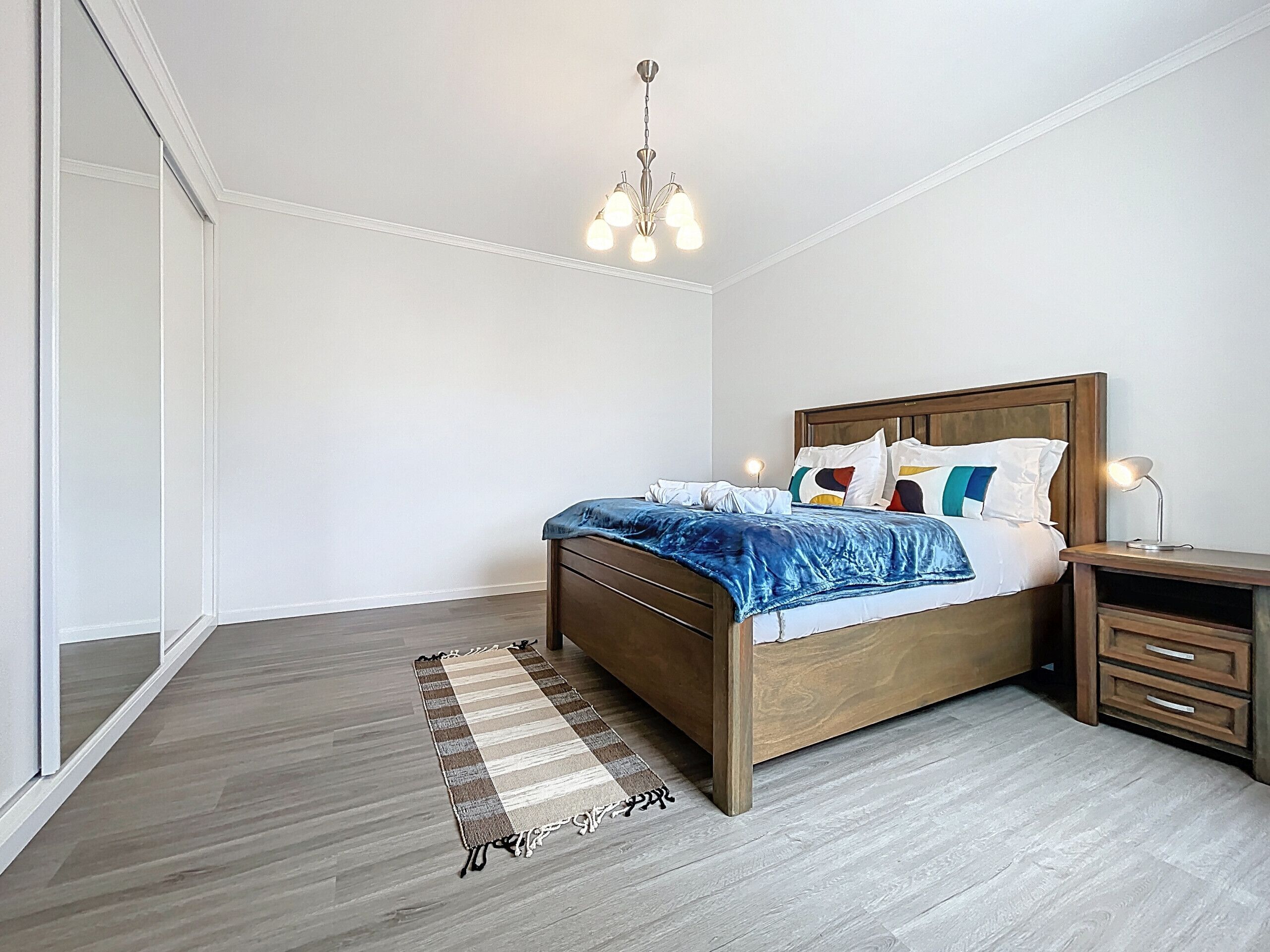 Un dormitorio con una cama de madera, una mesita de noche, una lámpara y un aplique colgante.