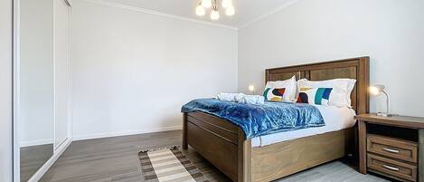 Un dormitorio con una cama de madera, una mesita de noche, una lámpara y un aplique colgante.