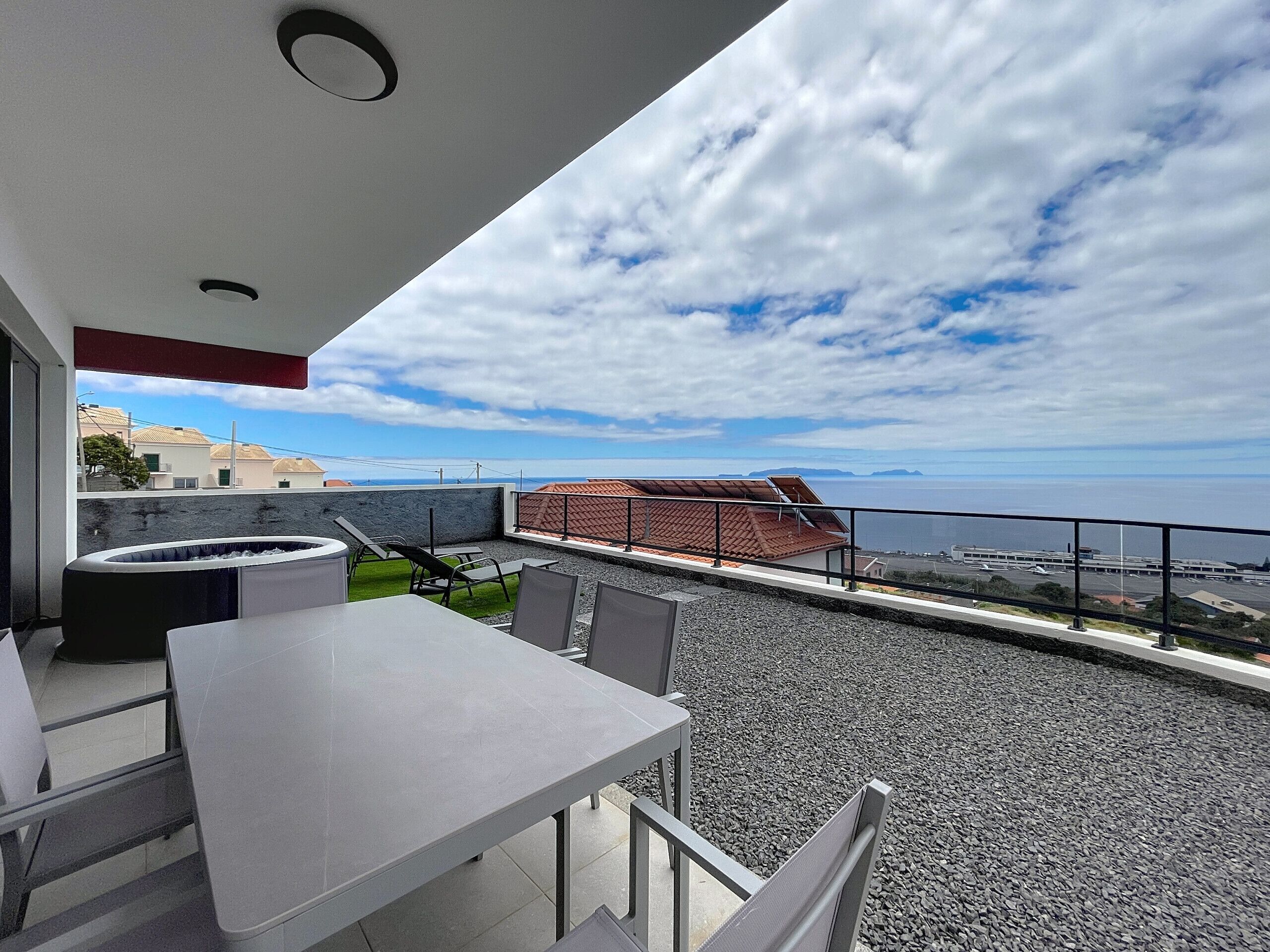 A terrace with a table and chairs, a small barbecue area, and a view of the sea and distant buildings.