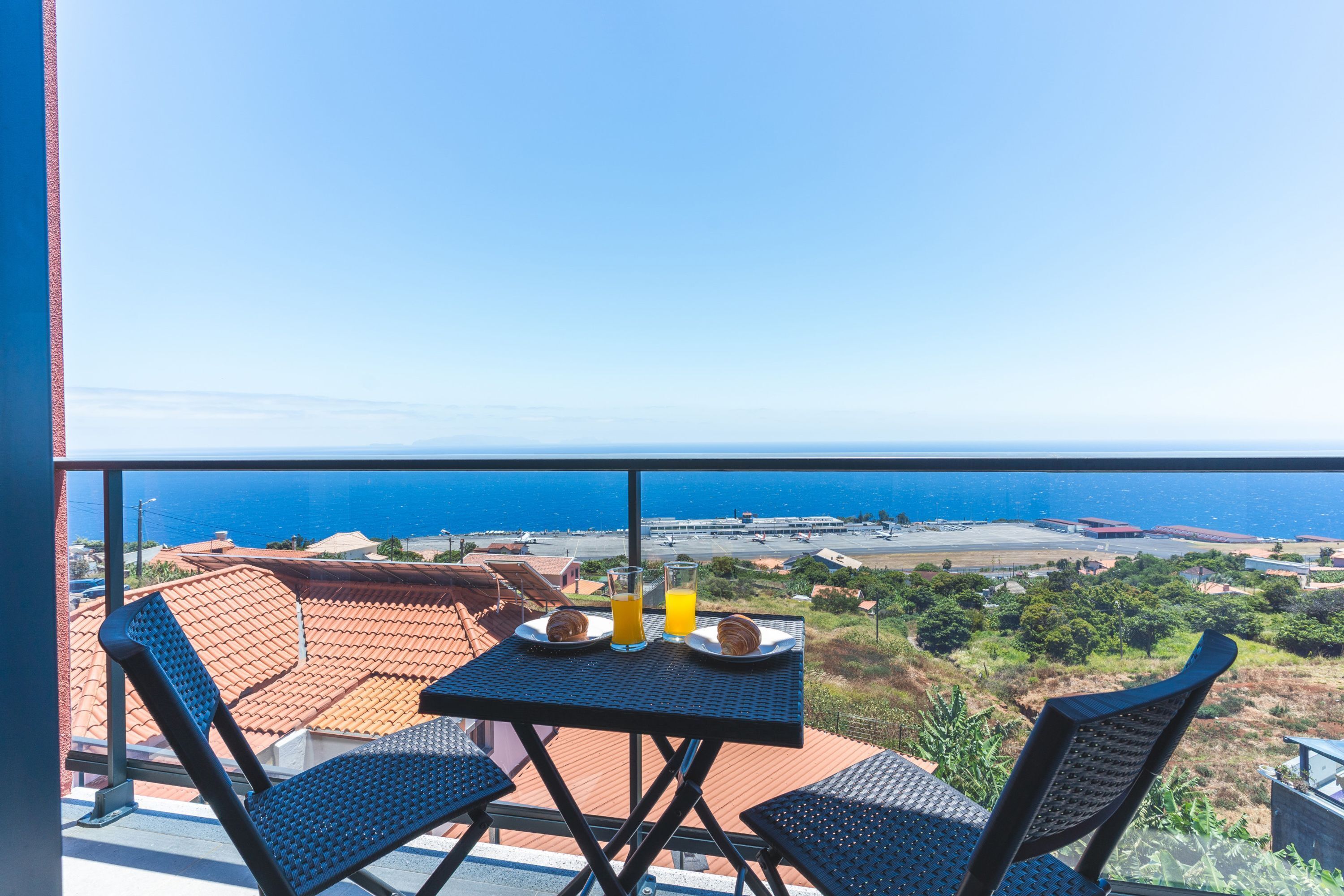 A balcony with a table set for breakfast, overlooking a coastal view.