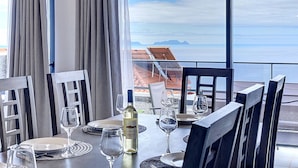 A dining table set with plates, glasses, and a bottle of wine, overlooking a scenic view of the ocean and mountains. - Blue Outlook View by Atlantic Holiday (Santa Cruz)