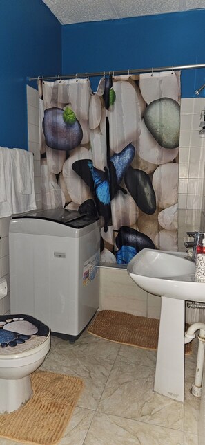 A bathroom with a blue wall, a shower curtain with a rock design, a white sink, and a toilet. - Cozy Spanish Town Hide-Away (Spanish Town)