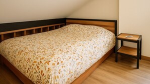 Una cama individual con una colcha estampada floral, una mesita de noche con un libro y suelo de madera.