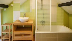 Un baño con tocador de madera, un lavabo blanco, ducha con mampara de vidrio y una bañera.