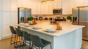 A modern kitchen with white cabinetry, stainless steel appliances, and a central island with bar stools. - Magical Dreams (Kissimmee)
