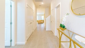 A hallway with white doors, a staircase, and a yellow console table with a plant. - Magical Dreams (Kissimmee)
