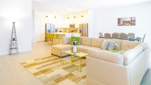 A modern living room with a beige sofa, a glass coffee table, and a yellow-striped rug. - Magical Dreams (Kissimmee)