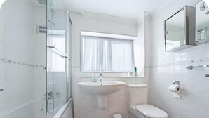 Une salle de bain moderne avec une douche à parois de verre, un lavabo, des toilettes et une fenêtre avec des rideaux.